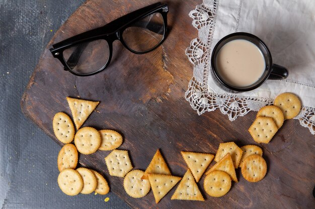 Vista superior de galletas saladas sabrosas con gafas de sol y una taza de leche en el escritorio de madera.