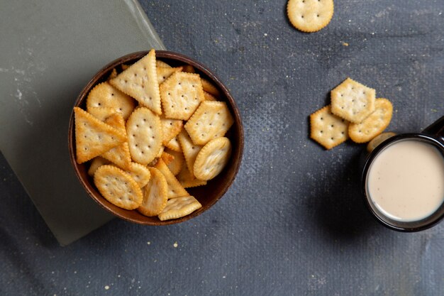 Vista superior galletas saladas sabrosas con una taza de leche en el refrigerio crujiente galleta de fondo gris