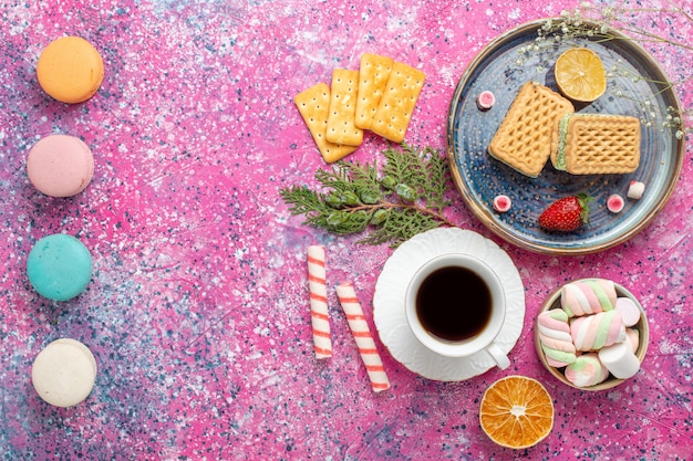 Vista superior de gofres dulces con taza de té y macarons en la superficie rosa