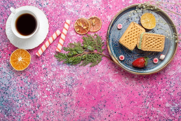 Vista superior de gofres dulces con taza de té en la superficie de color rosa claro