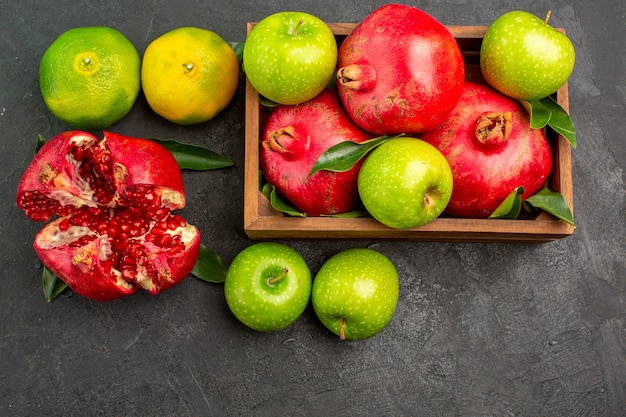 Vista superior de granadas frescas con mandarinas y manzanas en la superficie oscura de color de fruta madura