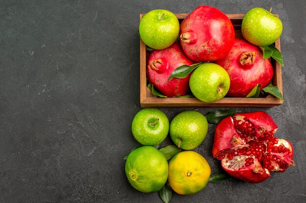 Vista superior de granadas frescas con mandarinas y manzanas en la superficie oscura frutas maduras de color