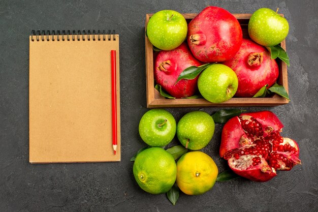 Vista superior de granadas frescas con manzanas y mandarinas en la superficie oscura de la fruta de color maduro