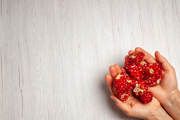 Vista superior de granadas rojas frescas en manos femeninas en el árbol de color de fruta de escritorio blanco
