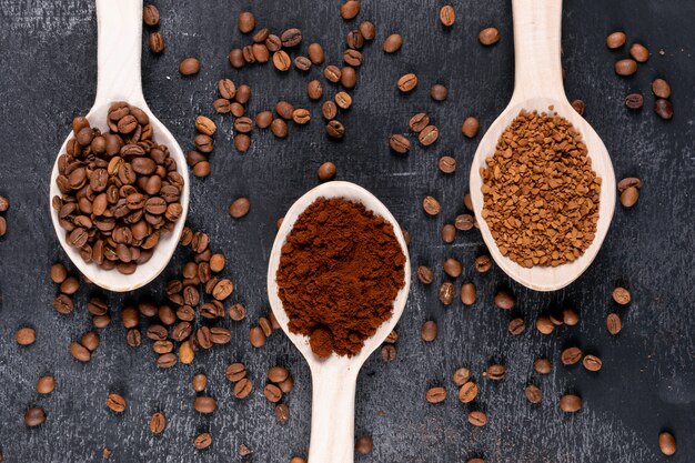 Vista superior de granos de café y café instantáneo en cucharas de madera sobre una superficie oscura