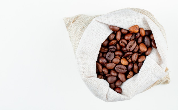 Vista superior de granos de café marrón en un saco sobre fondo blanco con espacio de copia
