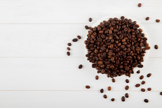 Vista superior de granos de café en un plato sobre fondo blanco con espacio de copia