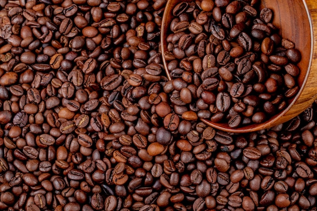 Vista superior de granos de café tostados dispersos de un tazón de madera sobre fondo de granos de café