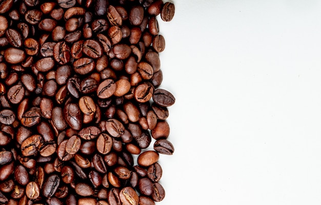 Vista superior de granos de café tostados esparcidos sobre fondo blanco con espacio de copia