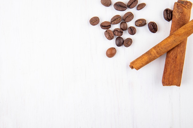 Vista superior de granos de café tostados y palitos de canela sobre fondo blanco de madera con espacio de copia