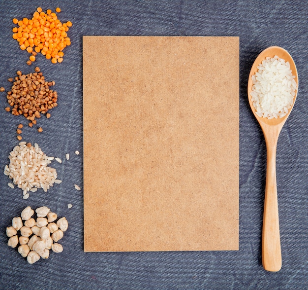 Vista superior de granos de cereales y semillas montones garbanzos arroz alforfón y lentejas rojas con hoja de papel marrón y una cuchara de madera sobre fondo gris