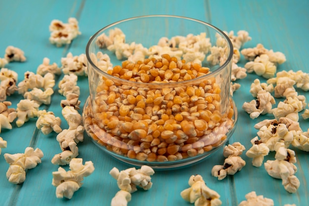 Vista superior de granos de palomitas de maíz en un recipiente de vidrio con palomitas de maíz aislado en una mesa de madera azul