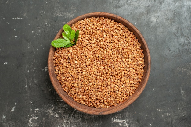 Vista superior de granos de trigo sarraceno con verde en un recipiente marrón sobre fondo gris