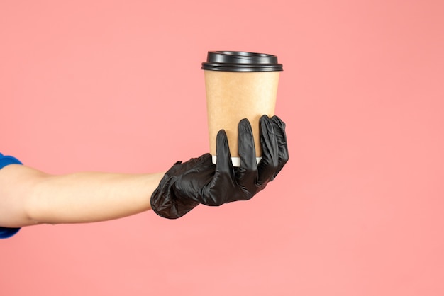 Vista superior del guante negro con mano sosteniendo una taza de delicioso café sobre fondo melocotón pastel