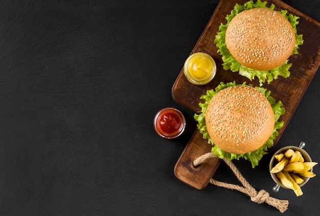 Vista superior de hamburguesas y papas fritas en tabla de cortar con espacio de copia