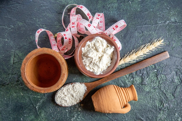 Foto gratuita vista superior de la harina dentro de una olla marrón con una cuchara de madera en el escritorio oscuro