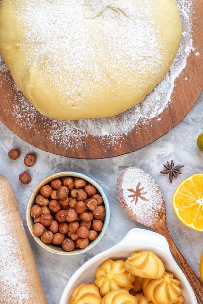 Foto gratuita vista superior de harina de hojaldre cruda en tablero redondo galletas de avellanas limón sobre fondo blanco manchado