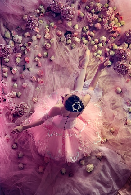 Vista superior de la hermosa joven en tutú de ballet rosa rodeada de flores