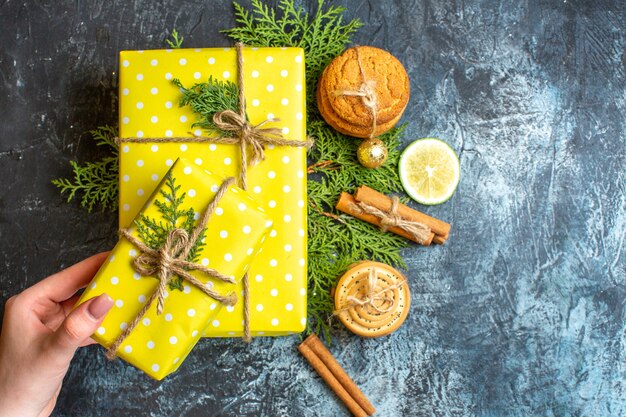 Vista superior de hermosas cajas de regalo amarillas en ramas de abeto galletas apiladas limones canela limón sobre fondo oscuro