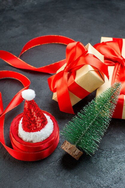 Vista superior de hermosos regalos con cinta roja y árbol de navidad sombrero de santa claus en una mesa oscura