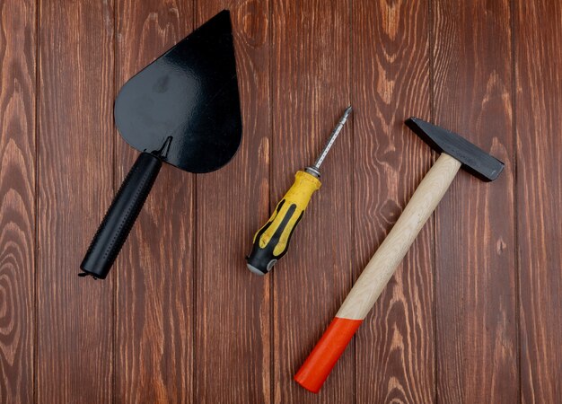 Vista superior de herramientas de construcción como destornillador llana y martillo de ladrillo sobre fondo de madera