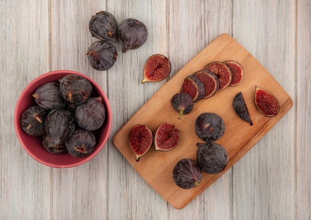 Foto gratuita vista superior de higos de misión negros maduros frescos en una tabla de cocina de madera con higos negros en un recipiente sobre una superficie de madera gris