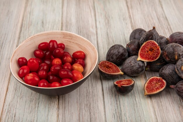 Vista superior de higos de misión negros maduros saludables con cerezas de cornalina en un recipiente sobre una pared de madera gris