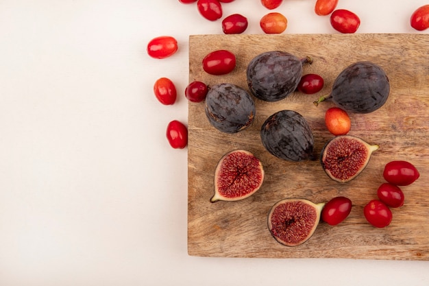 Vista superior de higos negros frescos en una tabla de cocina de madera con cerezas de cornalina aislado en una pared blanca con espacio de copia