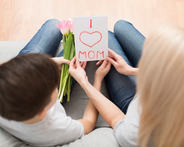 Vista superior hijo sorprendente madre con flores y tarjeta