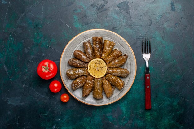 Vista superior de la hoja dolma deliciosa comida de carne oriental enrollada dentro de hojas verdes con tomates frescos en el escritorio azul comida de carne comida cena plato salud vegetal