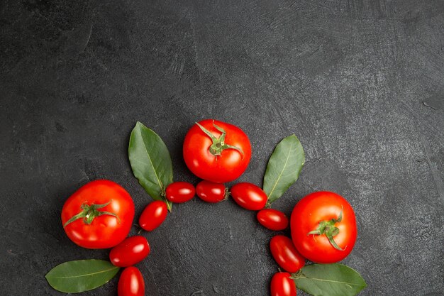 Vista superior de hojas de laurel de tomates cherry y rojos en la parte inferior del suelo oscuro con espacio de copia