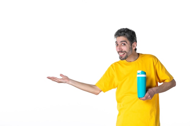 Vista superior del hombre joven feliz en camisa amarilla y mostrando termo azul apuntando algo en el lado derecho sobre fondo blanco.