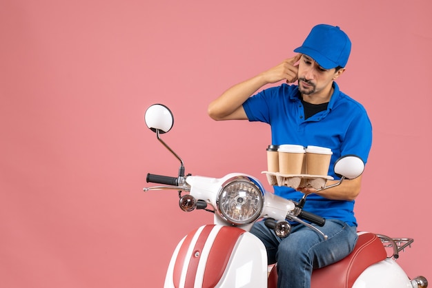 Vista superior del hombre de mensajería de pensamiento con sombrero sentado en scooter en melocotón pastel