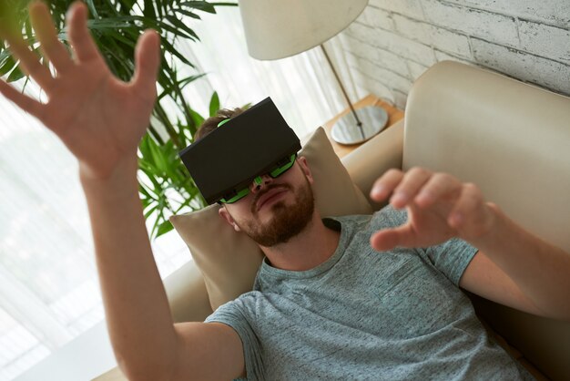 Vista superior del hombre probando la aplicación VR en el sofá de su casa