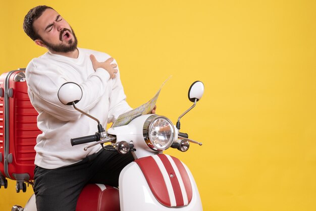 Vista superior del hombre con problemas sentado en la motocicleta con la maleta en él sosteniendo el mapa que sufre de un ataque al corazón sobre fondo amarillo aislado