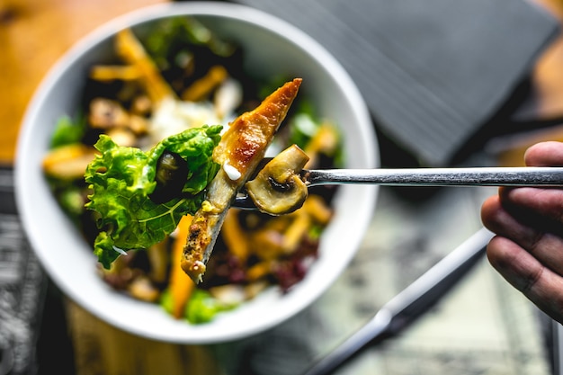 Vista superior, un hombre sostiene un tenedor con ensalada de pollo frito y champiñones