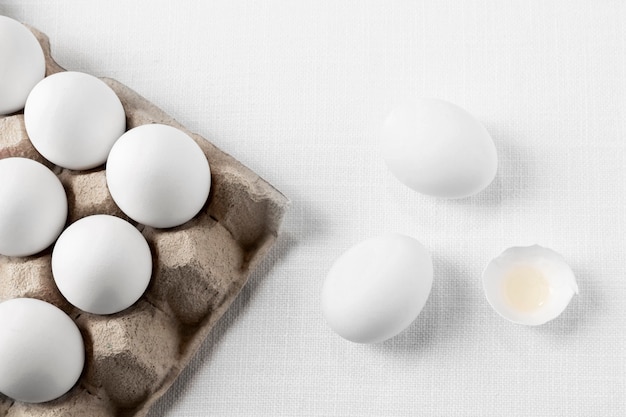 Vista superior de huevos blancos en cartón con cáscaras