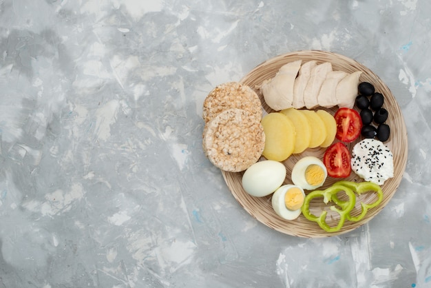 Vista superior huevos cocidos con aceitunas pechugas y tomates en gris, desayuno de alimentos vegetales