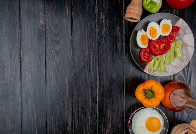 Vista superior de huevos cocidos en un plato con rodajas de tomate con vinagre de manzana sobre un fondo de madera con espacio de copia