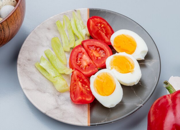 Vista superior de huevos cocidos en un plato con rodajas de tomates en un plato sobre fondo blanco.