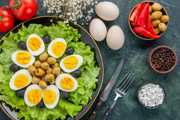 Vista superior de huevos cocidos en rodajas con ensalada verde y aceitunas sobre fondo oscuro