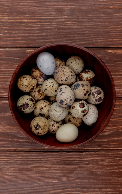 Vista superior de huevos de codorniz con cáscaras de color crema con manchas marrones en un recipiente de madera sobre un fondo de madera