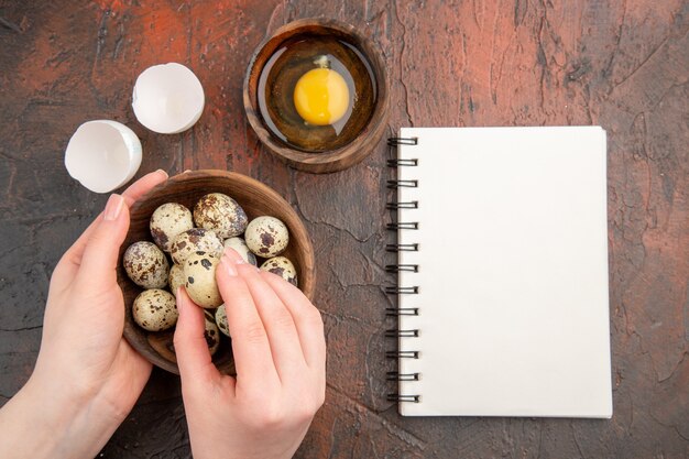 Vista superior de huevos de codorniz frescos con huevo crudo dentro de la placa sobre la mesa oscura