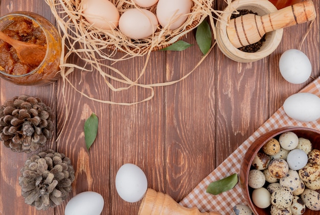 Vista superior de huevos de codorniz en un tazón de madera sobre tela marcada con huevos de gallina con piñas sobre un fondo de madera con espacio de copia