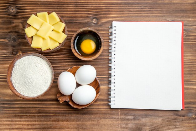 Vista superior de huevos crudos enteros con harina y queso en la mesa de madera marrón masa de huevo harina de pastelería polvo