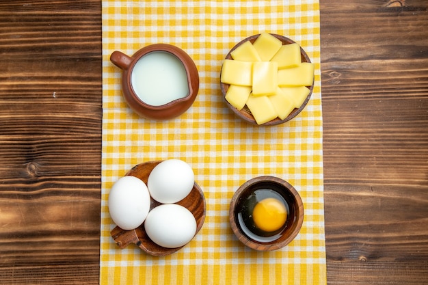 Vista superior de huevos crudos con queso en rodajas y leche en la superficie de madera producto huevos masa comida comida cruda