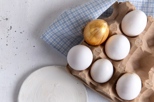 Vista superior de huevos enteros blancos con uno dorado sobre la superficie blanca