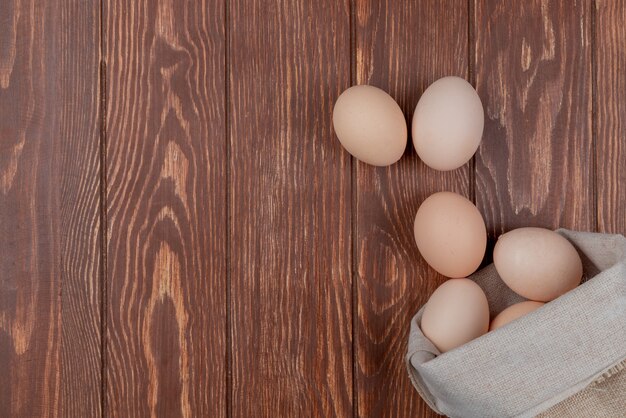 Vista superior de huevos frescos de color crema de pollo en una bolsa de arpillera sobre un fondo de madera con espacio de copia