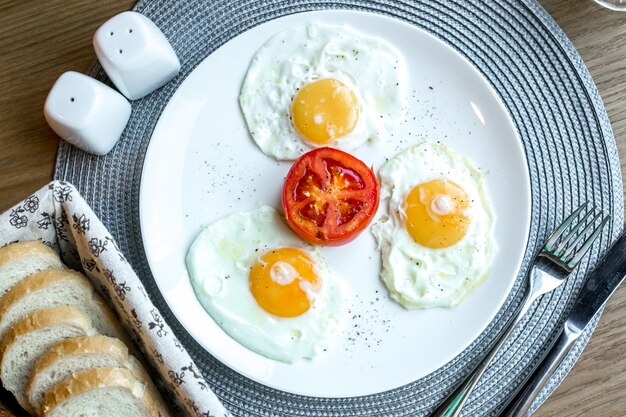 Vista superior huevos fritos con tomate en un plato con sal y pimienta sobre la mesa