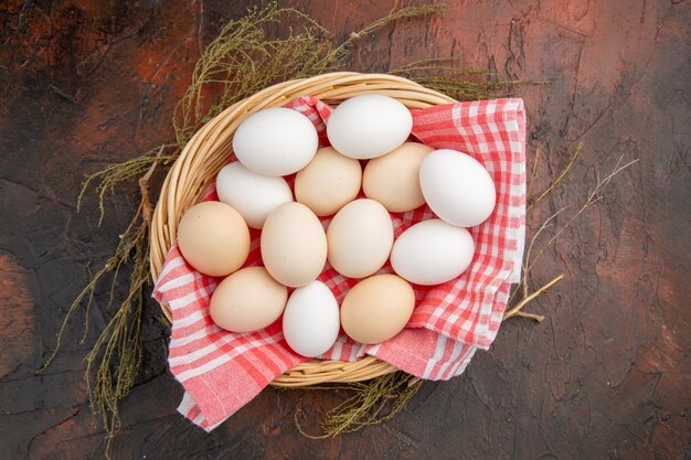 Vista superior de los huevos de gallina blanca dentro de la canasta con una toalla en la mesa oscura foto comida animal comida cruda color de la granja